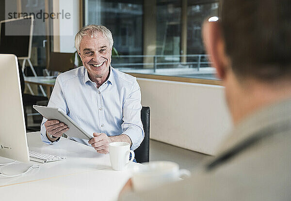 Glücklicher Geschäftsmann mit Tablet-PC diskutiert mit Kollegen im Büro