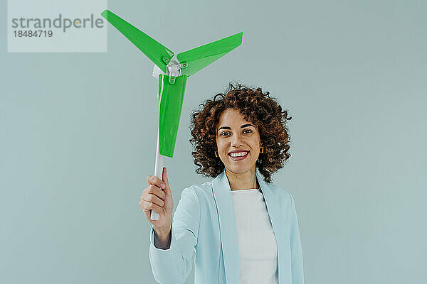 Happy woman with Afro hairstyle holding wind turbine model against colored background