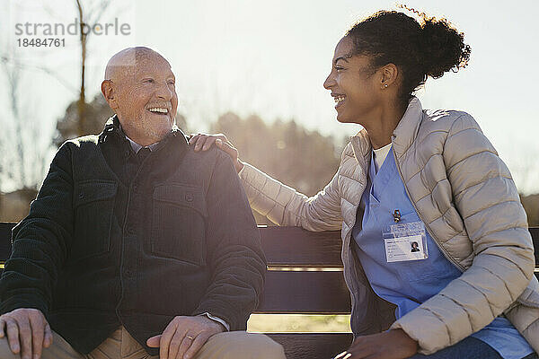Glücklicher älterer Mann  der an einem sonnigen Tag mit dem Hausmeister im Park sitzt