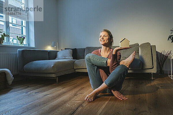Glückliche Frau mit Hausmodell beim Yoga im Wohnzimmer
