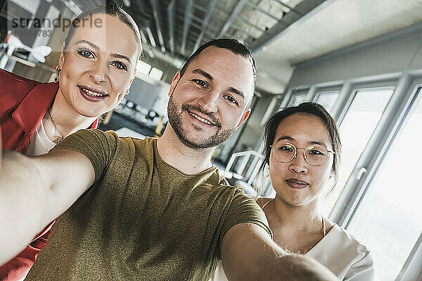 Lächelnder Geschäftsmann macht Selfie mit Kollegen im Büro