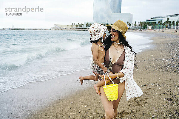 Glückliche Mutter trägt ihren Sohn und geht am Strand spazieren