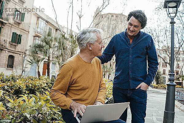 Lächelnder Sohn und Vater mit Laptop  der neben Pflanzen sitzt