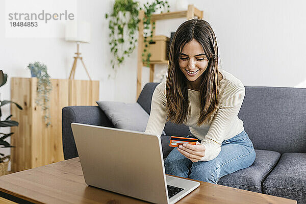 Glückliche Frau mit Kreditkarte beim Online-Shopping am Laptop zu Hause