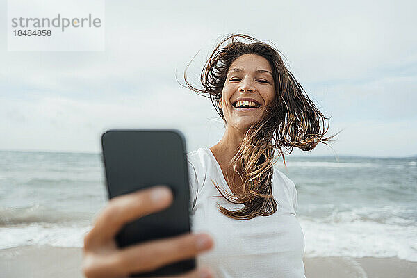 Fröhliche Frau  die am Strand ein Selfie mit ihrem Smartphone macht