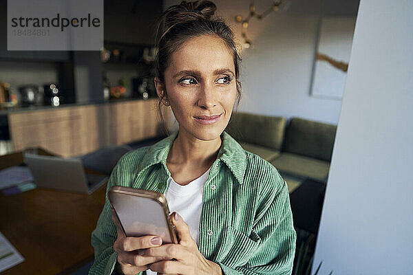 Nachdenkliche Frau mit Mobiltelefon im Heimbüro