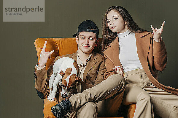Smiling teenage boy and girl with dog sitting in armchair
