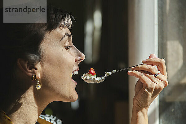 Junge Frau isst einen Löffel Erdbeeren und Sahne