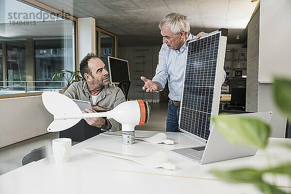 Geschäftsmann diskutiert mit Kollegen am Solarpanel über den Rotor einer Windkraftanlage im Büro