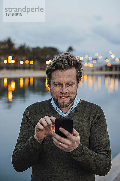 Glücklicher reifer Mann  der bei Sonnenuntergang sein Mobiltelefon benutzt