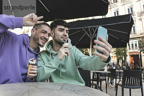 Glückliches schwules Paar mit Eis  das im Café ein Selfie mit dem Smartphone macht