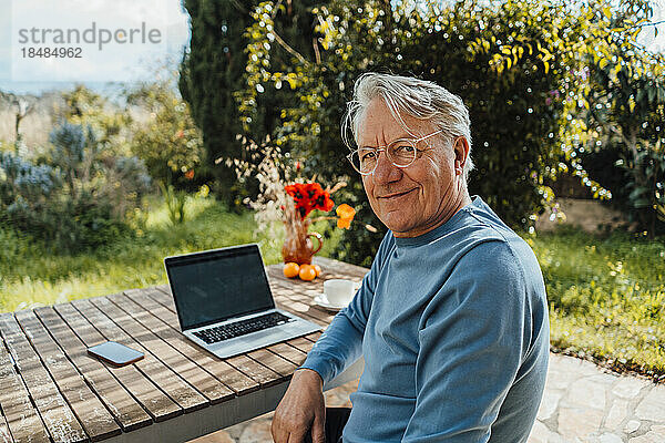 Lächelnder älterer Mann mit Laptop  der am Tisch sitzt