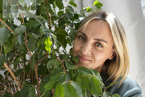 Lächelnde blonde Frau mit Pflanzen zu Hause