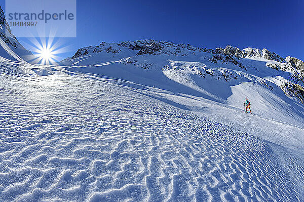 Austria  Tyrol  Female skier ascending slope in Zillertal Alps with sun shining in background