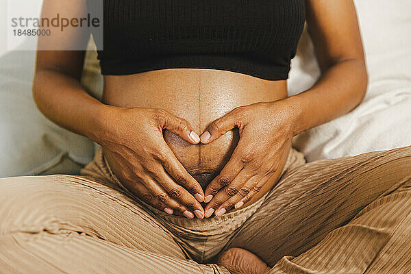 Schwangere Frau formt ein Herz mit den Händen auf dem Bauch