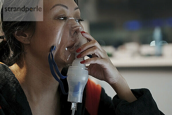 Woman inhaling through inhaler mask at home
