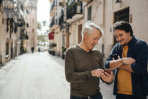 Lächelnder Mann diskutiert mit Vater über Smartphone auf der Straße