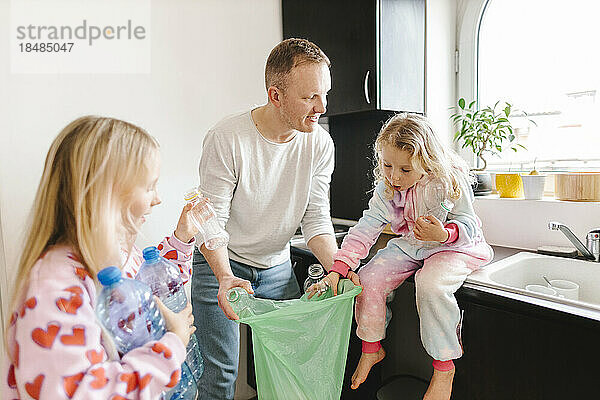 Lächelnder Vater recycelt Plastikflaschen mit Töchtern zu Hause