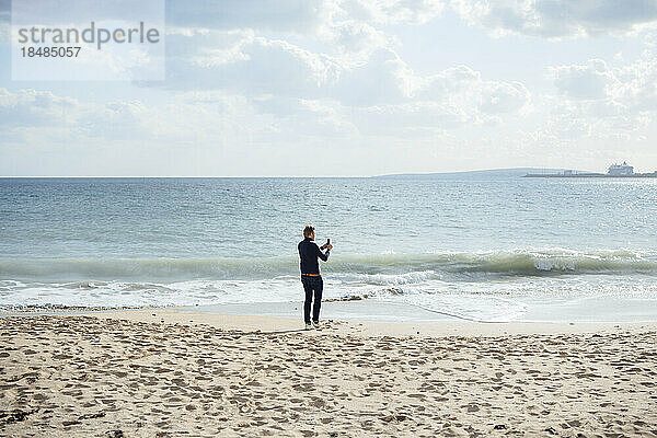 Mann fotografiert Meer mit Smartphone am Strand