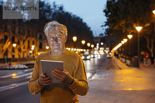 Lächelnder älterer Mann steht mit Tablet-PC am Fußweg