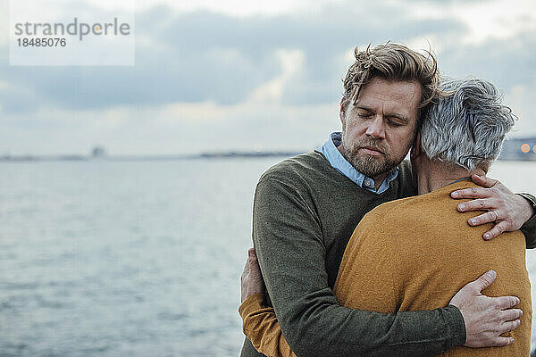 Reifer Mann mit Bart umarmt Vater vor dem Meer