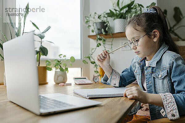 Nachdenkliches Mädchen mit Brille erledigt zu Hause Schulaufgaben