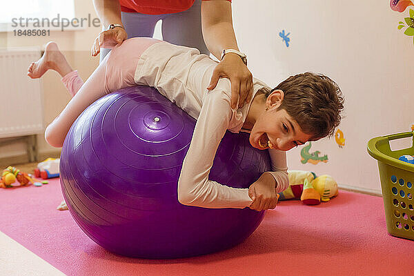 Physical therapist helping girl with disability in exercising on fitness ball at rehabilitation centre