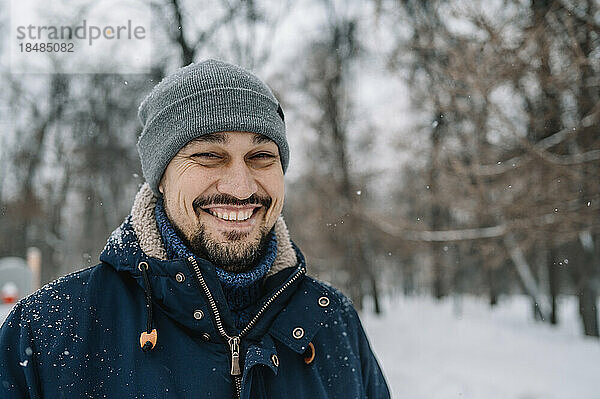Glücklicher Mann mit Strickmütze genießt den Schneefall