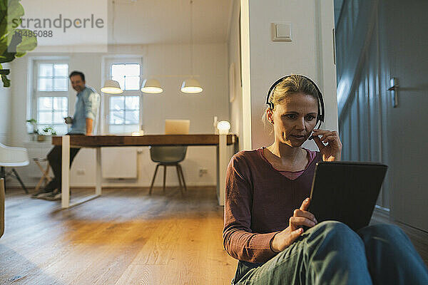 Frau benutzt Tablet-PC und spricht über Headset im Heimbüro
