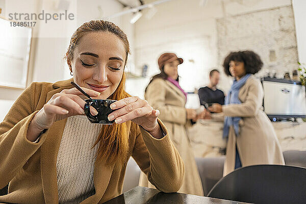 Lächelnde Frau hält Kaffeetasse in der Hand  Freunde stehen im Hintergrund