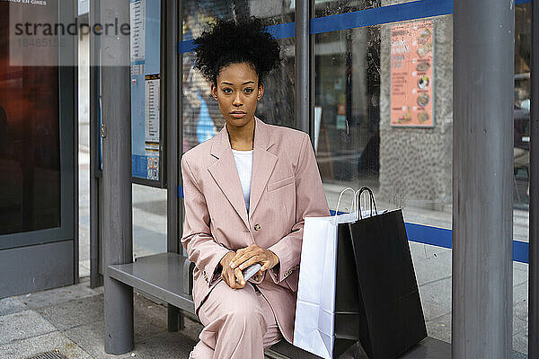 Nachdenkliche Geschäftsfrau sitzt mit Einkaufstüten auf der Bank