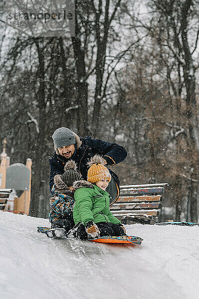 Vater und Jungen rodeln einen verschneiten Hügel hinunter