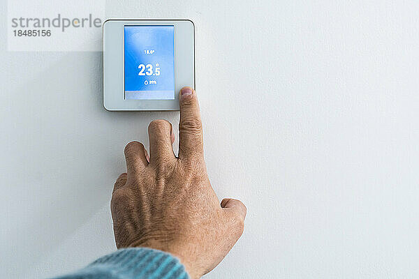 Hand eines Mannes  der den Thermostat an der Wand einstellt
