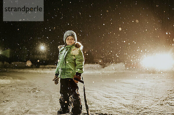 Netter Junge mit Strickmütze steht nachts im Schneefall