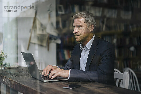 Reifer Geschäftsmann mit Laptop sitzt im Café