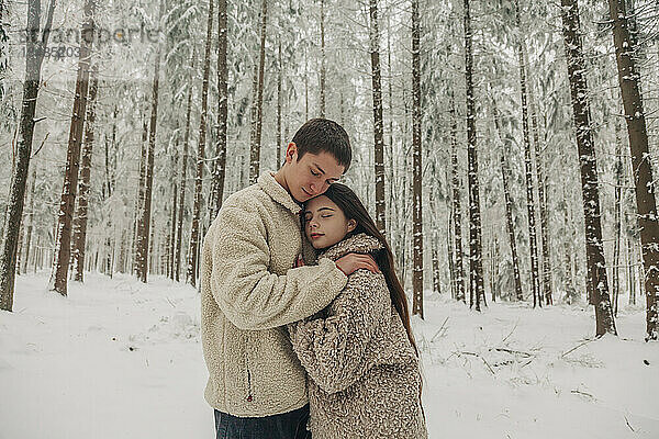 Teenage boyfriend hugging girlfriend in snowy forest