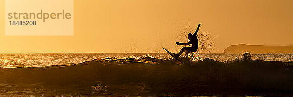 Silhouette eines Mannes  der bei Sonnenuntergang im Meer surft  Pembrokeshire  Wales