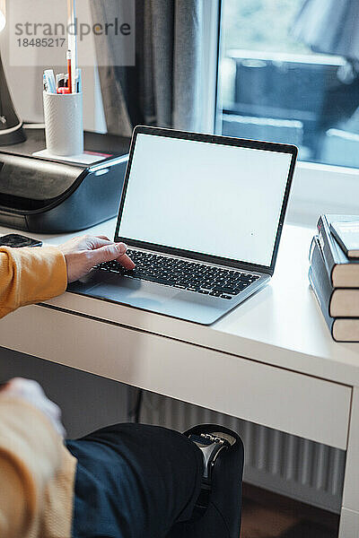 Junger Geschäftsmann mit Laptop sitzt zu Hause am Schreibtisch