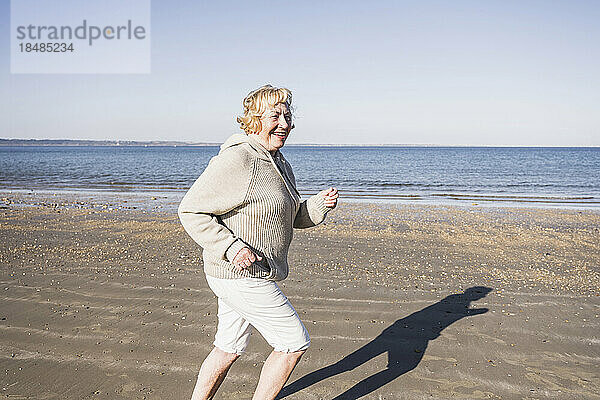 Lächelnde ältere Frau läuft im Urlaub am Strand über das Meer