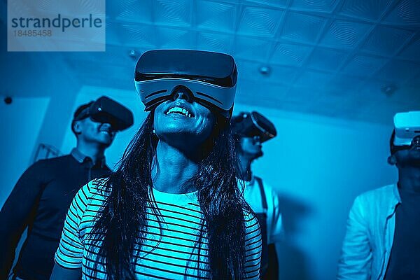 Gruppe junger Leute mit VR Brillen in einem Virtual Reality Spiel in einem blauen Licht  futuristisch oder Wissenschaft  Technologiekonzept spielen zusammen zu Hause