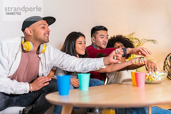 Gruppenbild von multiethnischen Freunden  die auf dem Sofa Popcorn essen und Limonade trinken. alle Popcorn essen