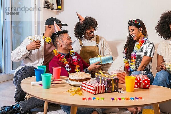 Gruppe von Freunden bei einer Geburtstagsfeier auf dem Sofa zu Hause  die lächelnd Geschenke überreichen