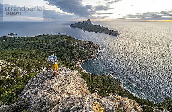 Ausblick auf Berge und Küste mit Meer  bei Sonnenuntergang  Wanderer auf einem Felsen  Wanderung nach La Trapa von Sant Elm  hinten Insel Sa Dragonera  Serra de Tramuntana  Mallorca  Spanien  Europa