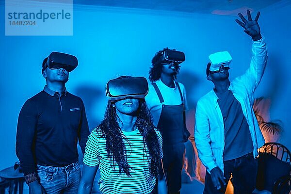 Gruppe junger Menschen mit VR Brille in einem Virtual Reality Spiel in einem blauen Licht  futuristisch oder Wissenschaft  Technologiekonzept erstaunt über den Realismus