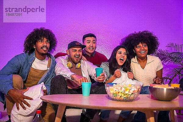 Party für Erwachsene. Junge Leute sitzen auf dem Sofa und schauen ein Fußballspiel mit Popcorn. Aufregung für Fußball  lila geführt  nervös in den letzten Minuten für das Spiel