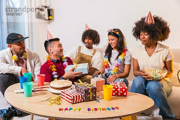 Gruppe von Freunden bei einer Geburtstagsfeier auf dem Sofa zu Hause  die lächelnd Geschenke überreichen