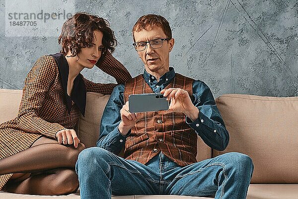 Ein Mann mittleren Alters zeigt seiner Frau  wie sie ihr intelligentes Haus über ihr Smartphone steuern kann
