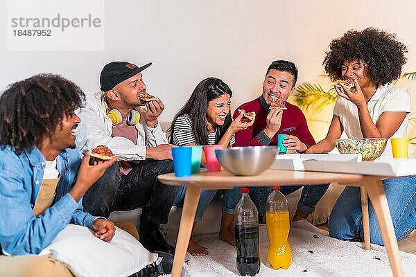 Eine Gruppe multiethnischer Freunde sitzt auf einem Sofa  isst Pizza und trinkt Limonade bei einer Hausparty  isst Pizza und erzählt lustige Geschichten