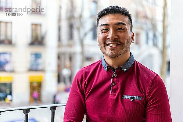Porträt eines jungen chinesischen Mannes auf einem Balkon zu Hause  lächelnd  Alltagssituation  Wohnung