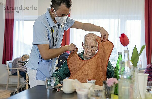 Pfleger legt einem Mann ein Lätzchen an im Pflegeheim  Heidelberg  Deutschland  Europa